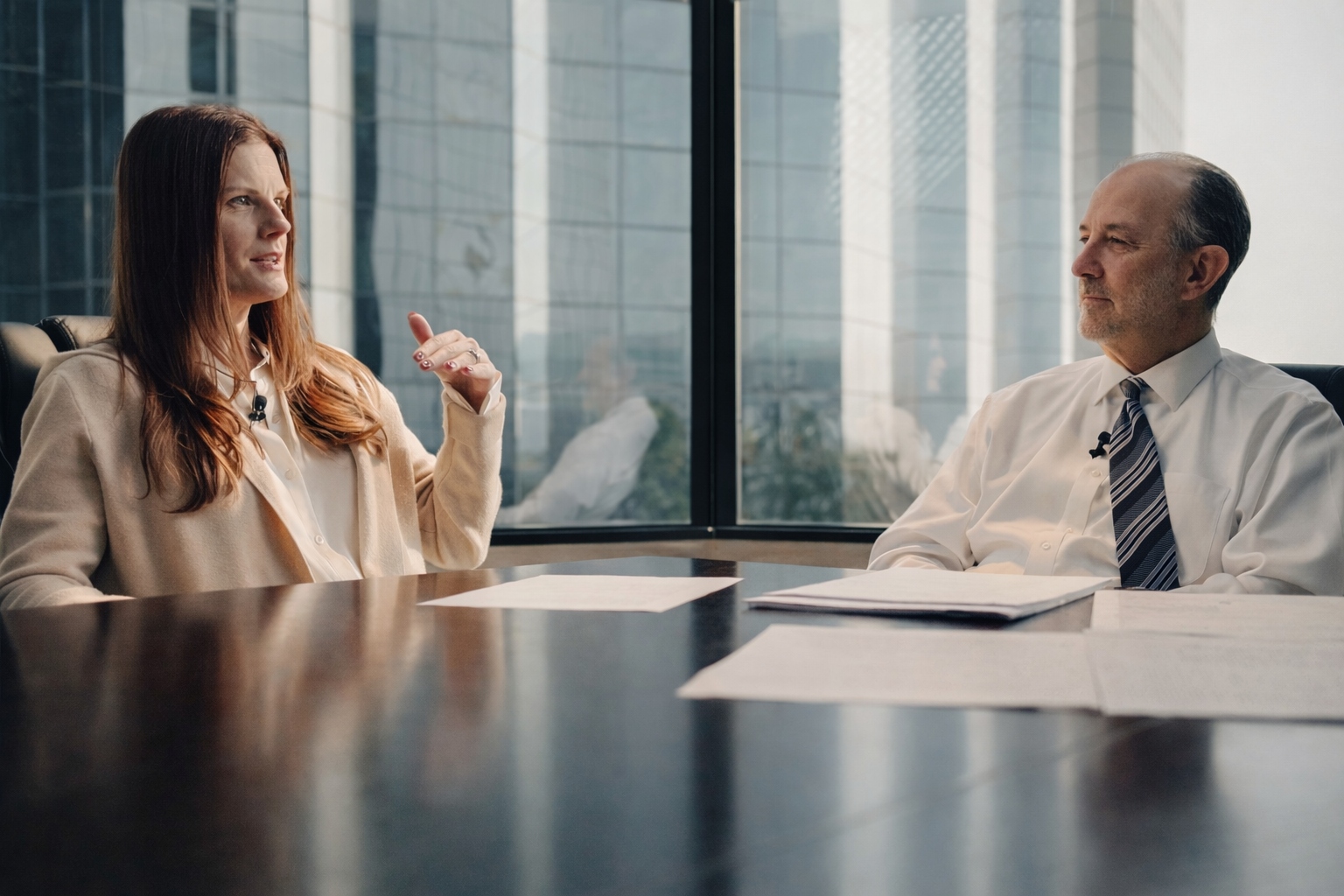 Female and male attorney discuss strategy at conference table in high-rise building.